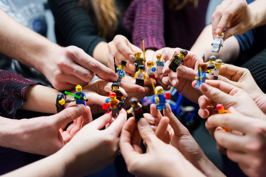 Many hands come together holding Lego people.
